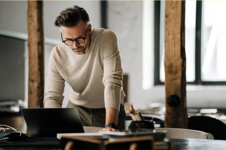 Professional man reviewing documents on a laptop in an office, ensuring data compliance.